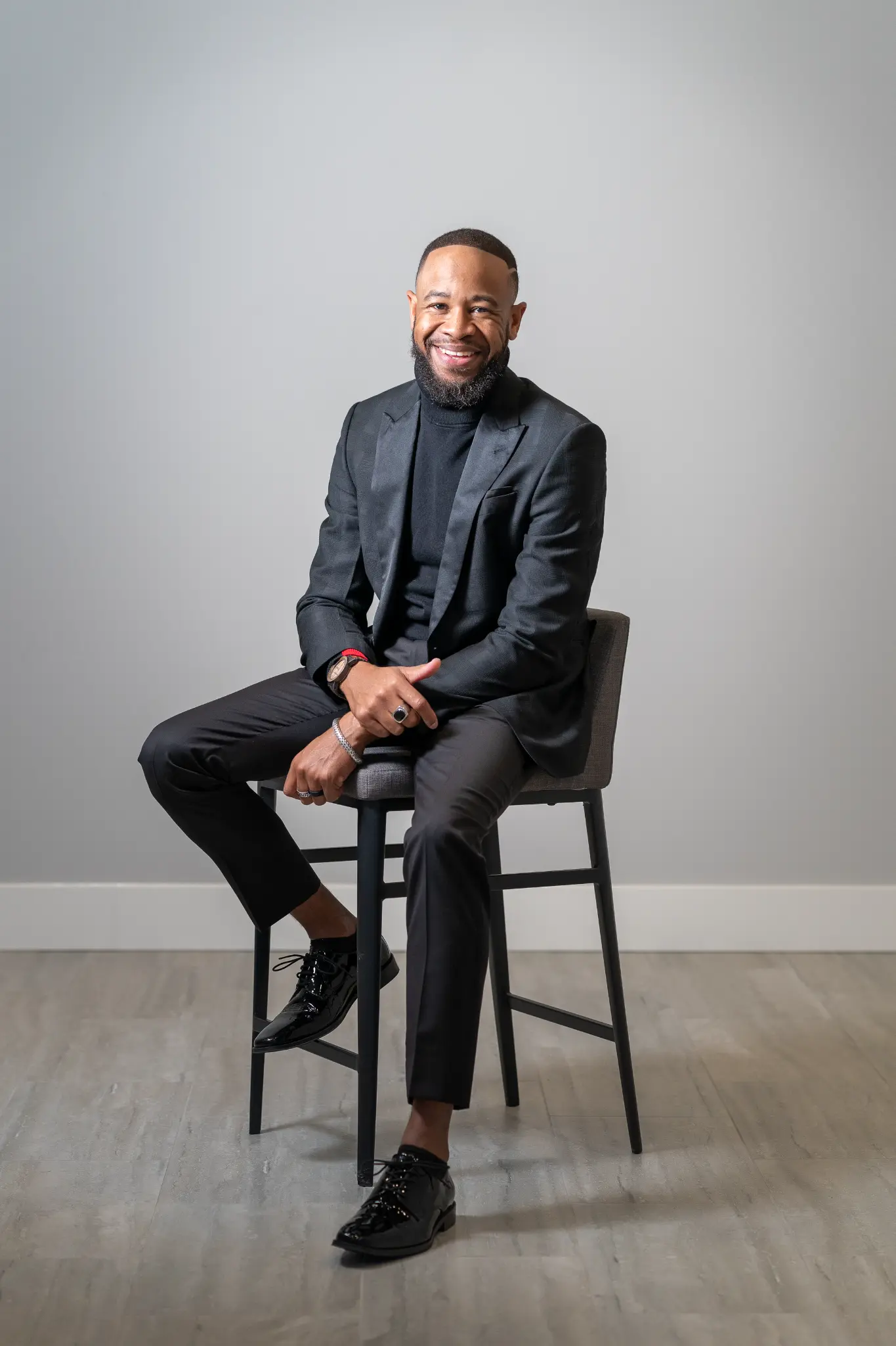 DeWayne Woods in black suit on high stool